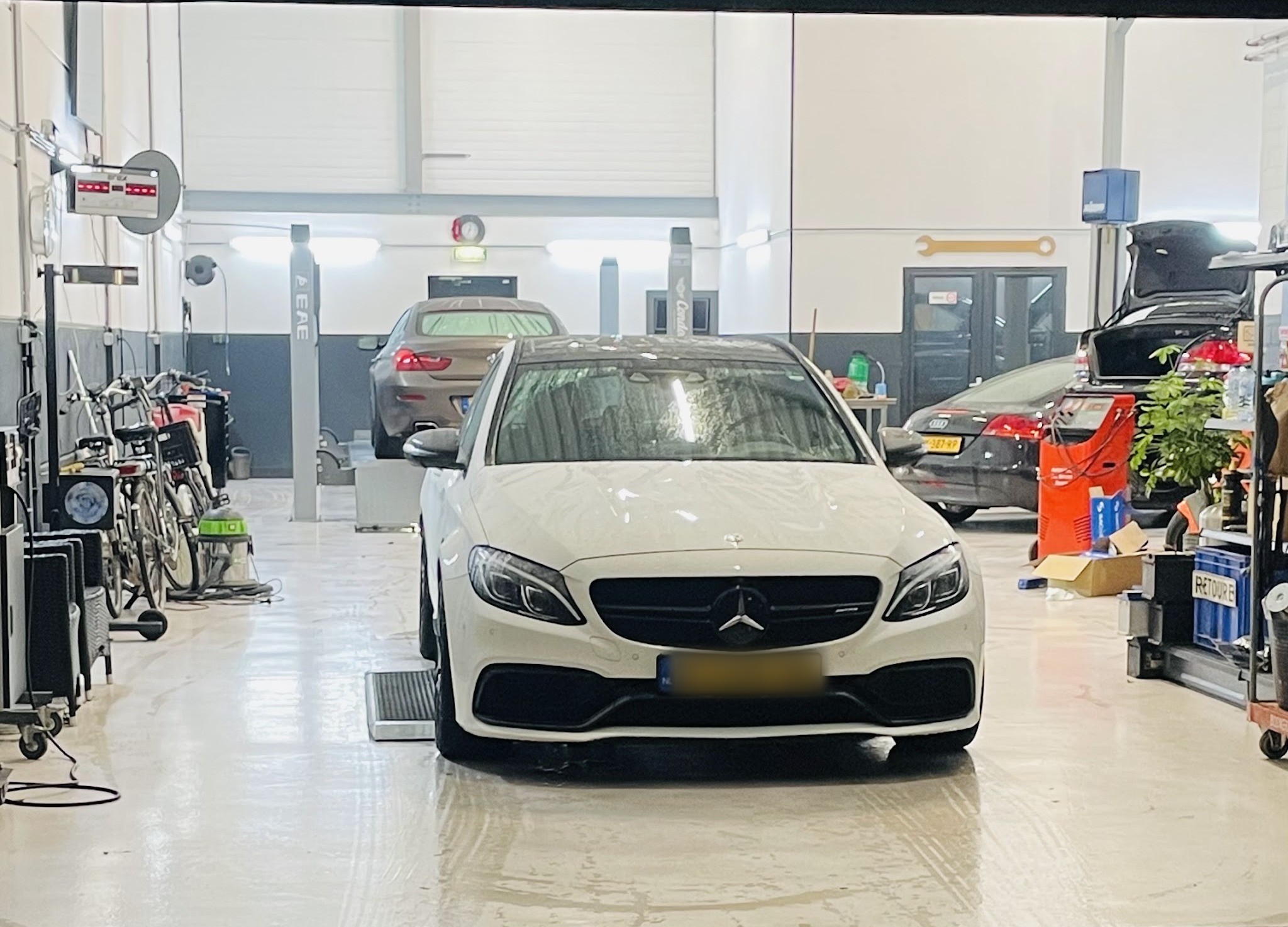 Een witte Mercedes in de werkplaats van Garage Schreuder, met werkbanken en gereedschapswagens