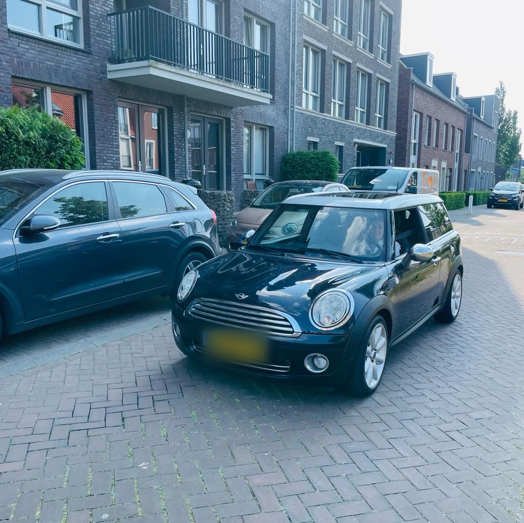 Zwarte Mini Cooper met wit dak, geparkeerd in een straat met nieuwbouw